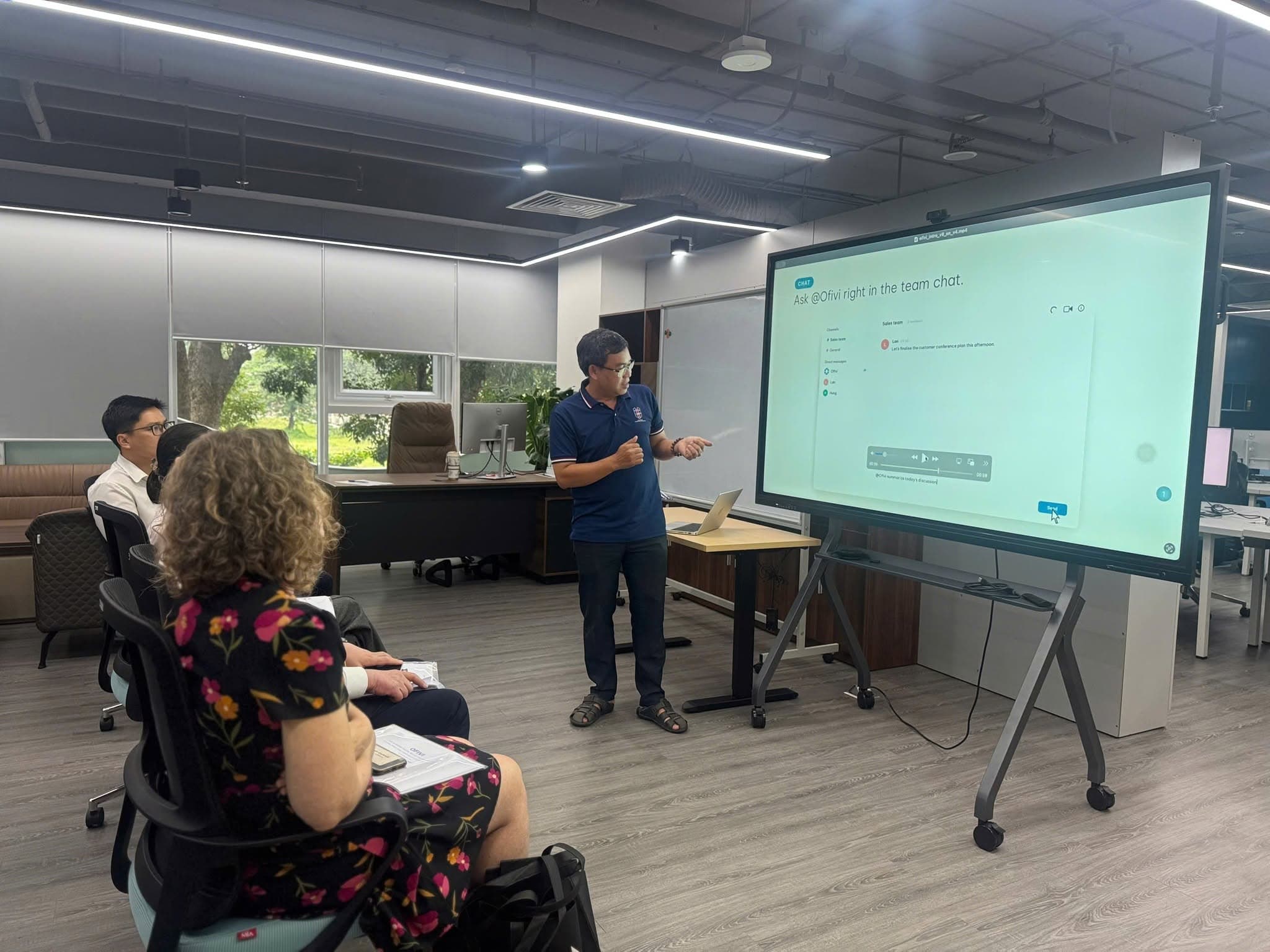 An AILOGY representative demonstrates interaction with the OFIVI assistant in a group conversation.